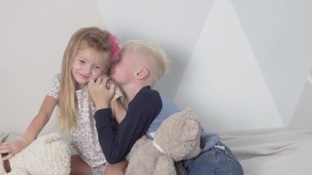Der Junge flüstert ihr eine lustige Geschichte von einem kleinen Mädchen ins Ohr — Stockvideo
