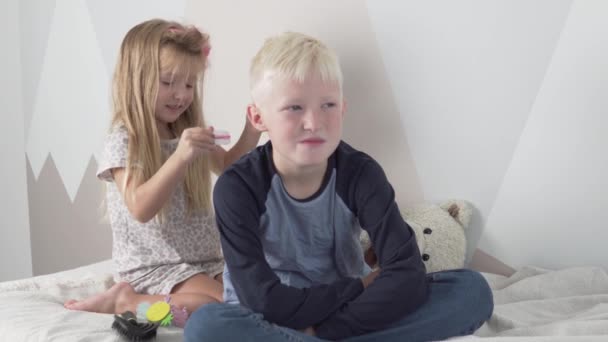 Divertida hermanita hace un peinado divertido al hermano mayor — Vídeo de stock