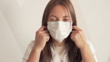 Güzel genç bir kadın doktor yüzündeki tıbbi maskeyi çıkarıyor.