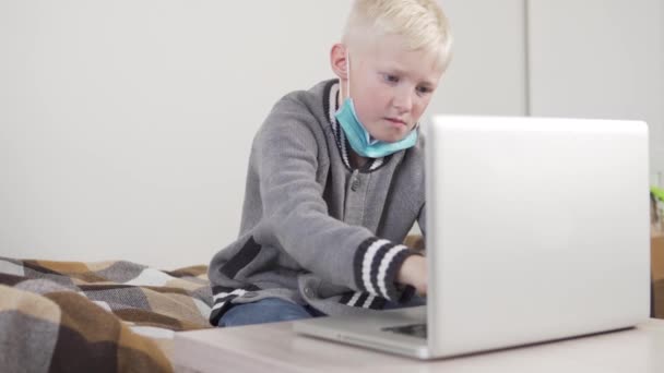 医療マスクの少年は、コンピュータ上の自宅で従事しています — ストック動画
