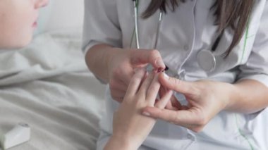 Doktor parmağını keserek oğlanın parmağını muayene eder.