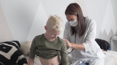 Bayan bir doktor, çocuk okula gönderilmeden önce bir çocuğun steteskopunu dinler.