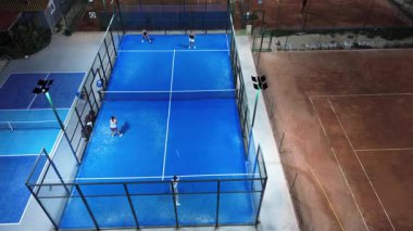 September 14, 2025, Spain, Alicante, Padel Club PAU5. Aerial drone view of a padel tennis court illuminated at night, with players engaged in a lively doubles match. The vibrant blue surface, bright