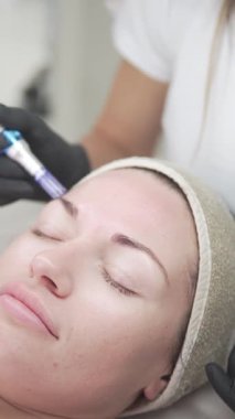 Vertical video of a woman undergoing a professional microneedling facial procedure at a beauty salon. The treatment stimulates collagen production, promoting skin rejuvenation, anti-aging benefits