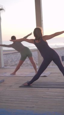 Vertical video of pregnant women practicing yoga on the beach at sunrise. Gentle stretching and mindful breathing create a peaceful atmosphere, combining prenatal fitness, wellness, and the beauty of
