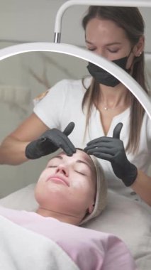 A beautician in gloves gently cleanses a woman is face before a skincare procedure at a professional beauty salon. This step ensures the skin is prepared and free of impurities for optimal treatment