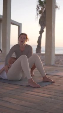 Dikey video, hamile bir kadın bir antrenörle plajda yoga yapıyor. Kalça Köprüsü Yapan Kız