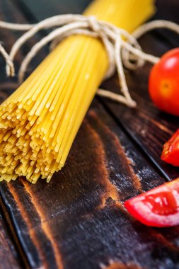 Ham İtalyan makarna spagetti ve koyu ahşap masa üzerinde domates