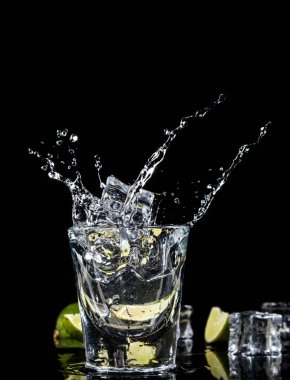 Meksika geleneksel tekila splash buz küpü kireç siyah zemin üzerine.