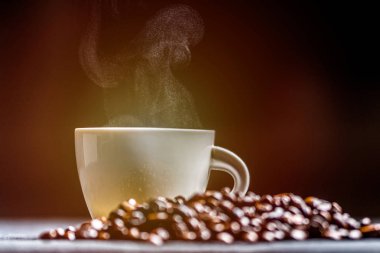 Beyaz turuncu ve koyu arka plan üzerinde duman ve kahve çekirdekleri ile sıcak kahve fincan