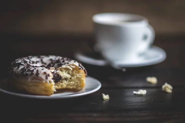 Een witte donut met chocolade strooi bijten — Stockfoto