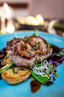 Izgara domuz pirzolası ya da pirzola, yarı buzlu, mavi tabakta koyun peynirli gnocchi.