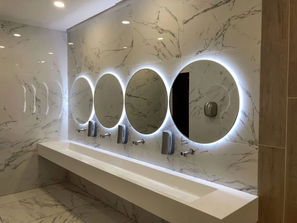 Mermer duvarlarda yuvarlak aynalar, beyaz lavaboların üzerinde. Beyaz restoran banyosu. İç dizayn. Banyo içi. 