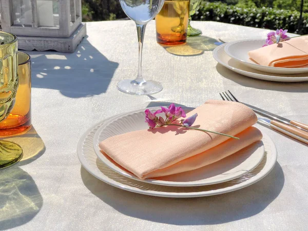 table set for dinner in garden. White table cloth. Rustic wedding table setting. Table decor and flowers.