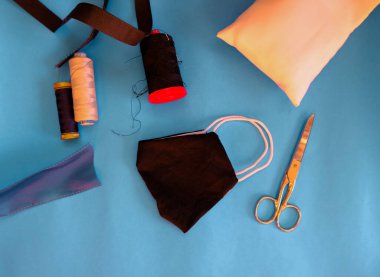 Mavi arka planda el yapımı tıbbi kumaş maske ekipmanları makaslar, kumaşlar, renkli iplikler. Dikiş araçları