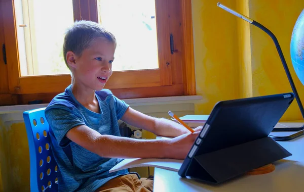 Sarışın beyaz çocuk internetten tablet / laptop kullanarak başkalarıyla konuşuyor. Çevrimiçi eğitim, uzaktan. Evde eğitim kavramı