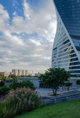 Şehir manzarası: modern yüksek binalar, bulutlu park ve gökyüzü.