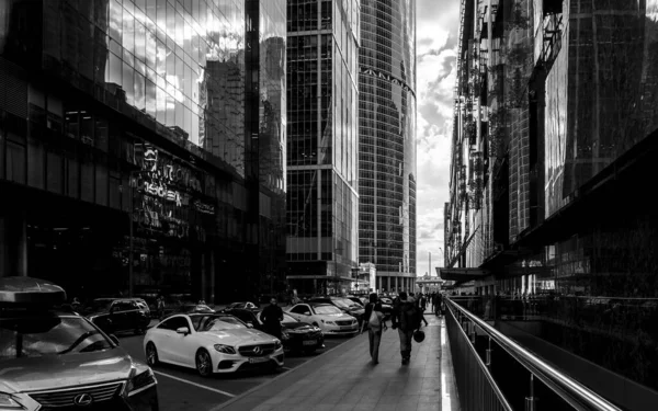 Les gens et les voitures dans la rue de la ville moderne avec des gratte-ciel. Photo noir et blanc. — Photo