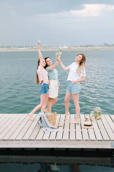 Τρία κορίτσια στέκονται σε μια ξύλινη προβλήτα μπροστά στο νερό. ανάπαυση, πικνίκ, λεμονάδα — Φωτογραφία Αρχείου