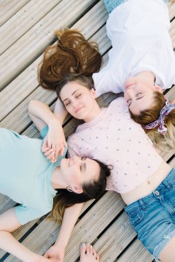 Üç kız, ahşap bir iskelede gözleri kapalı yatıyor. Dinlen, piknik