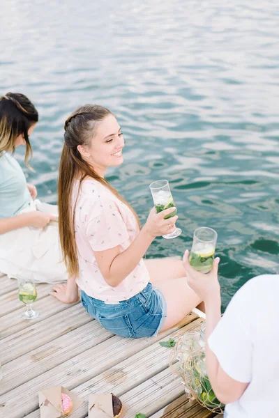 Schöne Mädchen, die auf einem Holzsteg in der Nähe des Sees sitzen. Ruhe, Picknick, Limonade — Stockfoto