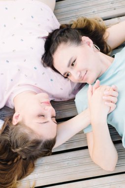 Kızlar ahşap bir iskelede uzanır ve el ele tutuşurlar. Dinlen, piknik.