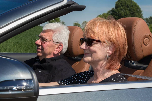 older couple drives with a luxury convertible car on a sunny day