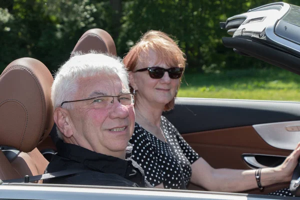 happy older couple drives with a luxury convertible car on a sunny day