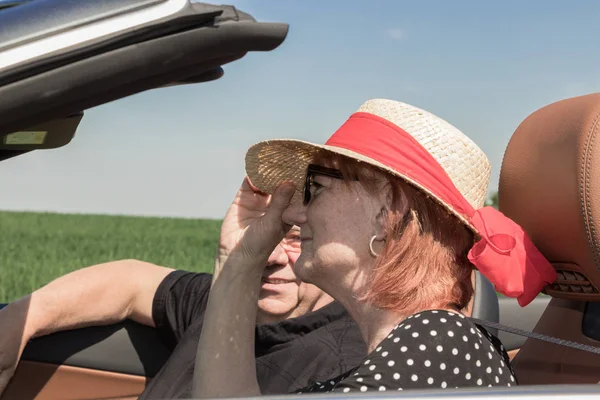 Beautiful older woman with a sun hat and her partner in a car