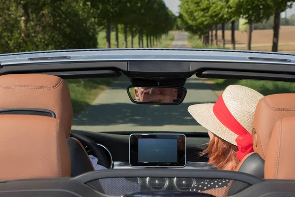 Older woman with sun hat and her partner in a convertible car