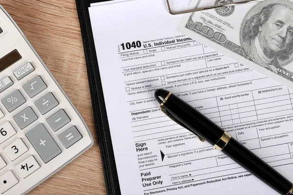 1040 tax form - individual income tax return form 1040 lies near hundred dollar bills, calculator and pen on a Table.