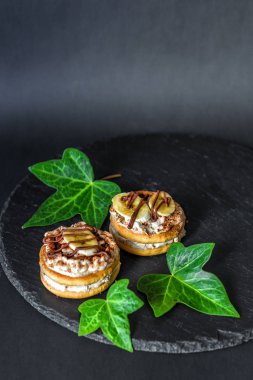 İki pasta bisküvi beyaz mascarpone krema, muz dilimleri ve çikolata, çikolata kerob tozu üzerinde siyah bir zemin üzerine kayrak bir yemek ile serpilir. Yeşil sarmaşık yaprakları ile süslenmiş. Ayrıntılı. Dikey olarak. Metin için boş alan.