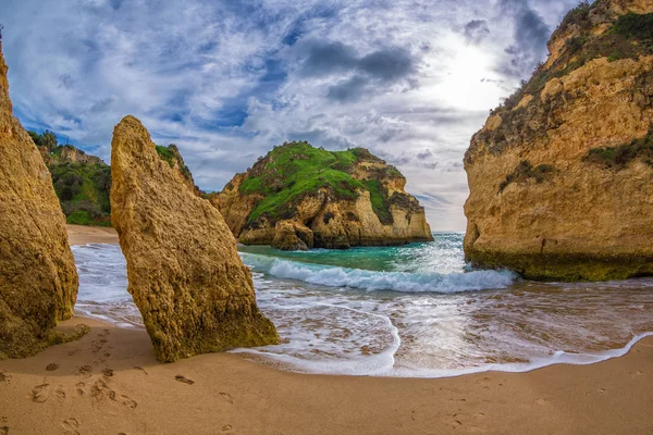 Ünlü kaya oluşumu bir koyda Alvor, Portimo, Algarve, Portekiz, Avrupa'nın Tres Irmaos plaj üzerinde. Praia dos, Tres Irmaos.The Güneş bulutların arasından parlıyor dalgalar kumsalda rulo. İki kayaların arasına görüntülemek