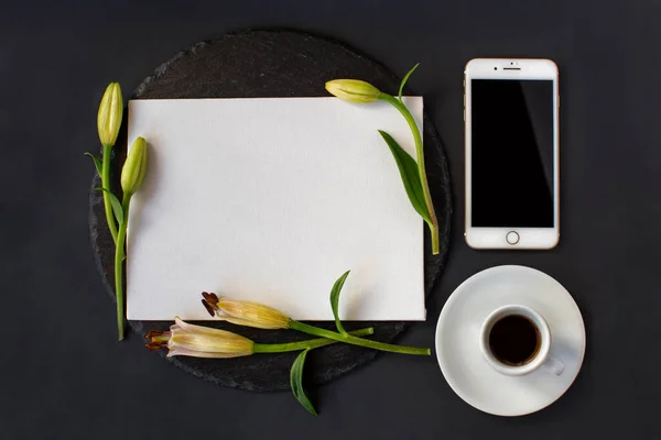 Bir fincan sade kahve, beyaz akıllı telefon ve siyah arka planda taze bahar çiçekleri tomurcuklanmış masajsız beyaz pankart. Romantik şık spa restoranı çerçevesi. Hayat düzdü. Üst Manzara. Spa