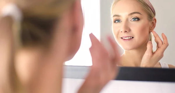 Жінка піклується про її красиву шкіру на обличчі, що стоїть біля дзеркала — стокове фото