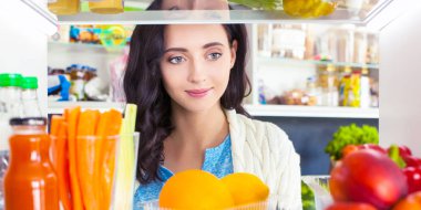 Sağlıklı yiyecek, sebze ve meyvelerle dolu açık buzdolabının yanında duran kadın portresi. Kadın portresi