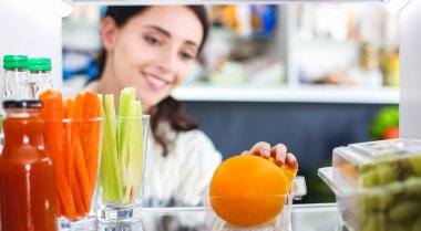 Sağlıklı yiyecek, sebze ve meyvelerle dolu açık buzdolabının yanında duran kadın portresi. Kadın portresi