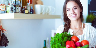 Mutfakta elinde sebzelerle gülümseyen genç bir kadın. Gülümseyen genç kadın