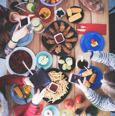 Ahşap masada otururken birlikte yemek yiyen bir grup insanın üst düzey görüntüsü. Masada yemek var. İnsanlar fast food yiyor..