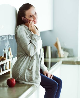 modern mutfakta otururken cep telefonu kullanan kadın.