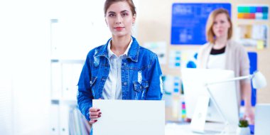 Masanın yanında duran iki genç kadın enstrüman, plan ve dizüstü bilgisayarla.