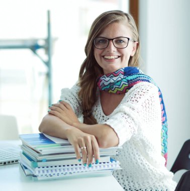 Kitapların arasında bir masada oturan genç bir kadın. Öğrenci