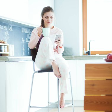 modern mutfakta otururken cep telefonu kullanan kadın.