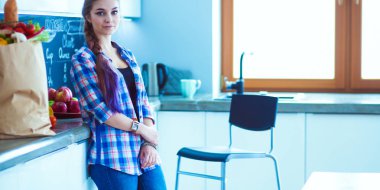 Kollarını mutfak arka planında kavuşturmuş genç bir kadının portresi..