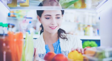 Sağlıklı yiyecek, sebze ve meyvelerle dolu açık buzdolabının yanında duran kadın portresi. Kadın portresi