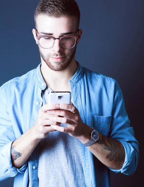 Smiling young man holding phone while text messaging — Stock Photo, Image