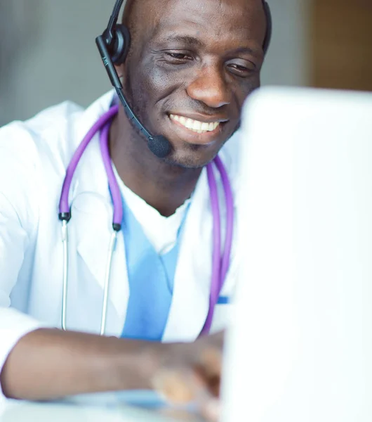 Portrait of young male doctor wearing headset while using computer at desk in clinic. Doctor. — Stock Photo, Image
