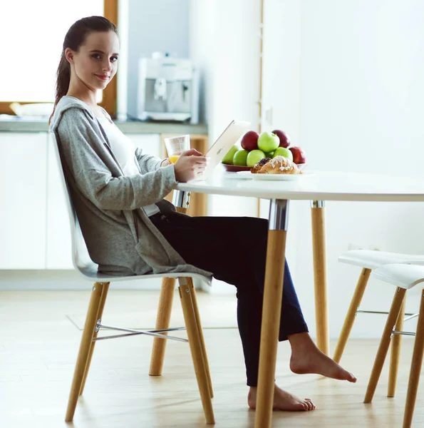 Mujer joven con jugo de naranja y tableta en la cocina. — Foto de Stock