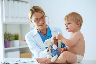 Kadın doktor, klinikte steteskoplu bir çocuğu dinliyor.