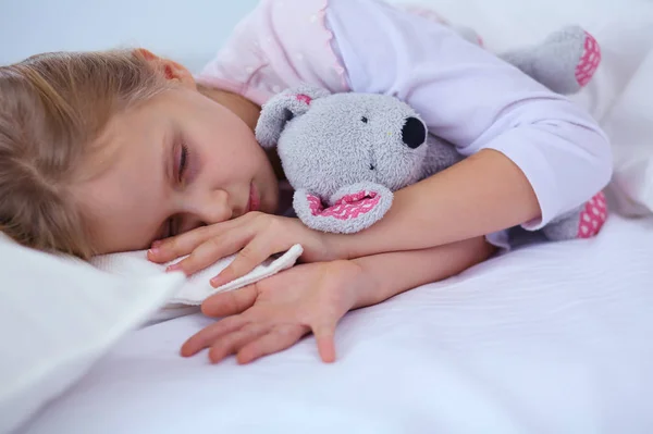 Bambino bambina dorme nel letto con un orsacchiotto giocattolo . — Foto Stock